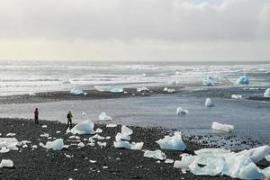 Menschen stehen am Rande des Jokulsarlon-Sees in Island mit verstreutem Eis auf der Oberfläche 65 foto