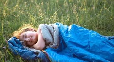 ein kind schläft in einem schlafsack auf dem gras bei einem campingausflug - umweltfreundliche erholung im freien, gesunder lebensstil, sommerzeit. süßen und friedlichen Schlaf. Mückenstiche, Abwehrmittel. foto