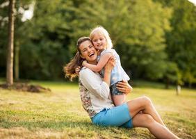 Porträt der glücklichen Mutter und des kleinen Mädchens, das im Park umarmt foto