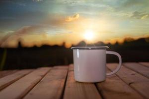 kaffeetasse auf dem holztisch mit dem sonnenaufgang hintergrund. weicher fokus. foto
