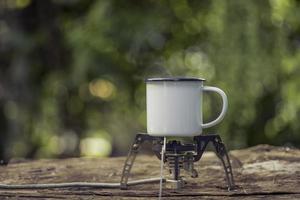 weiße emaille-kaffeetasse auf dem gasherd grüner wald bokeh hintergrund.vintage-stil. foto