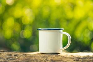 weiße emaille-kaffeetasse auf dem gasherd grüner wald bokeh hintergrund.vintage-stil. foto