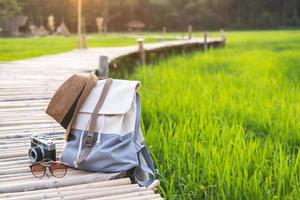 Rucksack mit Hut und Kamera auf Bambusweg am grünen Reisfeld, Reisekonzept foto