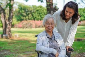 pflegekraft hilft und unterstützt asiatische seniorin oder ältere alte dame patientin im rollstuhl im park, gesundes starkes medizinisches konzept. foto