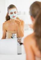 junge Frau, die Gesichtsmaske im Badezimmer anwendet