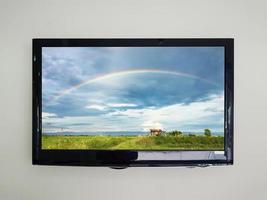 LED-Fernseher auf dem Wandhintergrund mit Regenbogen am Himmel über dem Landwirtschaftsfeld auf dem Fernsehbildschirm foto