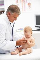 ein lächelnder Kinderarzt, der einem Baby ein Stethoskop hält foto