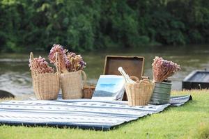 Buch- und Blumenkörbe auf blauer Matte mit Fluss und Wald im Hintergrund. Urlaubskonzept. foto