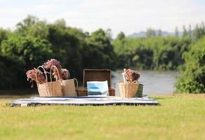 Buch- und Blumenkörbe auf blauer Matte mit Fluss und Wald im Hintergrund. Urlaubskonzept. foto