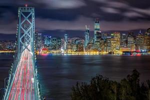 Panoramablick auf die Skyline von San Francisco und den Pier mit Autospuren über die Bay Bridge am Abend, Kalifornien, USA foto