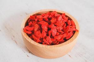 getrocknete chinesische Wolfsbeeren oder chinesisches Kraut der Goji-Beere oder Eherebe in der hölzernen Schaufel auf Holzschale isoliert auf Holzhintergrund. ausgewählten Fokus. foto