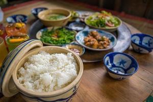 vietnamesisches familienkochset für vier personen gekochter reis, gemüsesuppe und gebratener fisch, gebratene zwiebeln mit hähnchen, gurkenscheibe, traditionelles vietnamesisches gericht auf dem land. foto