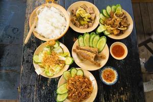 vietnamesisches familienkochset für vier personen gekochter reis, gemüsesuppe und gebratener fisch, gebratene zwiebeln mit hähnchen, gurkenscheibe, traditionelles vietnamesisches gericht auf dem land. foto