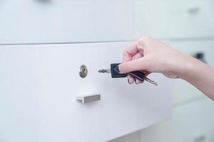 frauen halten den schwarzen einfachen schlüssel in der hand, um den weißen kleiderschrank zu öffnen. klaren Hintergrund. foto