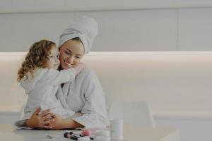 Mutter und süße kleine Tochter in weißen Bademänteln umarmen und genießen das Wochenende zusammen zu Hause foto