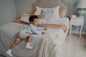 Fröhliches kleines afroamerikanisches Kind, das die Spielzeit drinnen auf dem Bett genießt foto