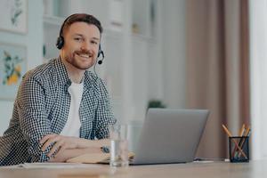 junger männlicher arbeiter, der laptop verwendet, während er zu hause arbeitet foto