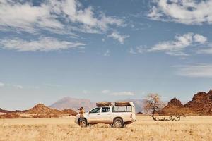 Fotograf in der Nähe des Autos, das sich in den Wüsten Afrikas, Namibia, befindet foto