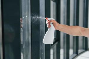 Nahaufnahme der Hand des Mannes, die eine Flasche mit Waschflüssigkeit hält. Fenster putzen foto