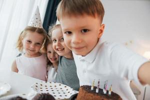 mit Kuchen. Selfies machen. Geburtstag feiern. Gruppe von Kindern ist tagsüber zusammen zu Hause foto