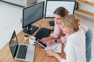 mit Telefon. Zwei weibliche Börsenmakler in formeller Kleidung arbeiten im Büro von PC foto