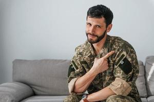 Soldat in Uniform ist drinnen im Wohnraum. auf dem Sofa sitzen foto