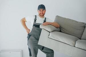 Anheben des Sofas. Der Handwerker arbeitet drinnen im modernen Raum foto