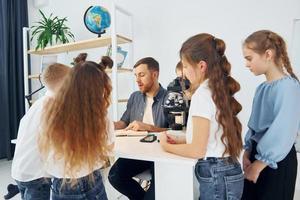 Konzeption des Biologieunterrichts. Mikroskop verwenden. gruppe von kinderschülern im unterricht in der schule mit lehrer foto