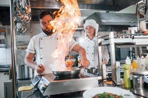 Flammen in der Bratpfanne. professioneller koch, der essen in der küche zubereitet foto