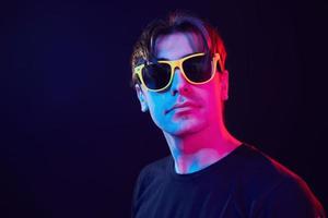 in gelber Sonnenbrille. mann, der im studio mit neonlicht steht foto