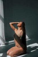 schönes sonnenlicht und frau. model in unterwäsche mit schlankem körpertyp posiert im studio foto