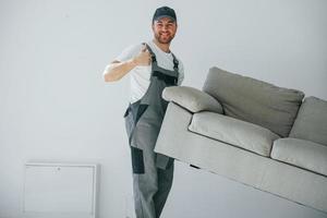 Anheben des Sofas. Der Handwerker arbeitet drinnen im modernen Raum foto