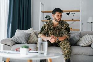 auf dem Sofa. Posttraumatische Belastungsstörung. Soldat in Uniform sitzt drinnen foto