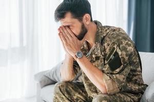 Flashbacks haben. Posttraumatische Belastungsstörung. Soldat in Uniform sitzt drinnen foto