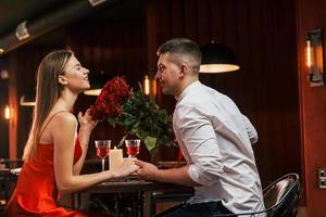in rotem Kleid und weißem Hemd. Romantisches Paar isst im Restaurant zu Abend foto