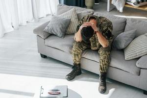 schlechte Laune. Posttraumatische Belastungsstörung. Soldat in Uniform sitzt drinnen foto