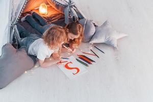 Brief schreiben. Konzeption von Lernen und Bildung. Zwei kleine Mädchen sind zusammen im Zelt im Wohnraum foto