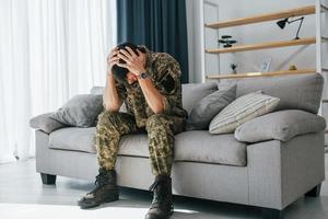 Posttraumatische Belastungsstörung. Soldat in Uniform sitzt drinnen foto