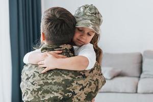einander umarmen. Soldat in Uniform ist mit seiner kleinen Tochter zu Hause foto