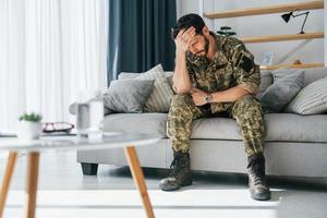 Posttraumatische Belastungsstörung. Soldat in Uniform sitzt drinnen foto