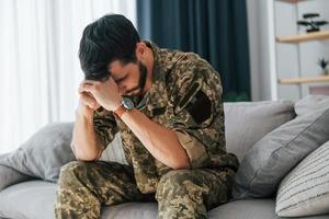 Posttraumatische Belastungsstörung. Soldat in Uniform sitzt drinnen foto