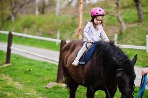 Kleines Mädchen im rosafarbenen Sturzhelm reitet Pony. foto