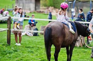 Kleines Mädchen im rosafarbenen Sturzhelm reitet Pony. foto