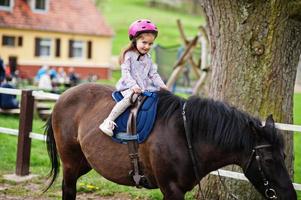 Kleines Mädchen im rosafarbenen Sturzhelm reitet Pony. foto