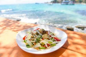 Papaya-Salat mit blauer Krabbe auf Tisch und Strand Meer Küste Hintergrund thailändisches Essen rohe Krabbe würziger Salat Meeresfrüchte und Gemüse auf dem Meer-Konzept foto