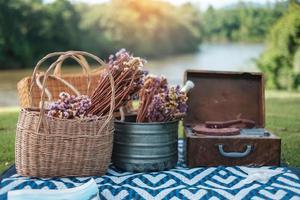 picknickset im park in der nähe des flusses, getrocknete blumen, körbe, weinflasche, buch und retro-schallplatte. Sommer-, Frühlings- und Urlaubskonzept foto