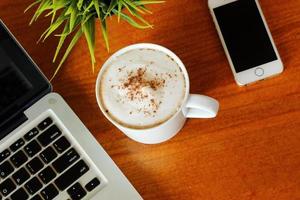 Laptop mit heißem Latte und Smartphone auf Holztisch von oben. foto