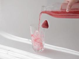 menschliche Hand, die eine Flasche mit Erdbeersaft hält foto