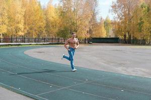 sportlicher Mann ohne Hemd, der in der Herbstsaison auf einem Stadion joggt. foto