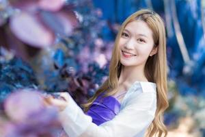 asiatische frau, die bronzehaarige trägt, weißes hemd und ein lila hemd lächelt glücklich im blau getrockneten blumengarten als hintergrund. foto